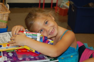 Girl leaning on desk with school supplies.