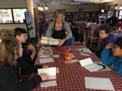 Teacher serves tray of books to students in library